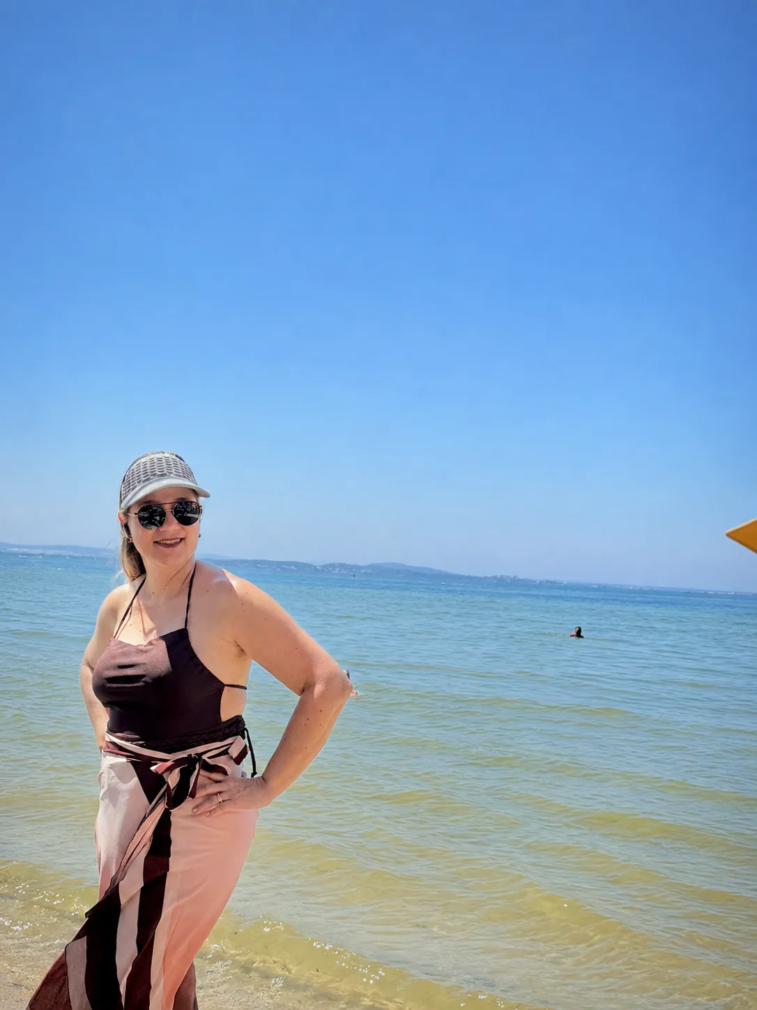 Michelle sorrindo na praia, de viseira e óculos escuros, com o mar ao fundo